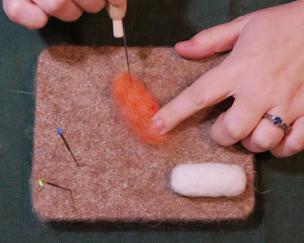 Salmon orange wool being shaped with a felting needle to resemble a piece of salmon.