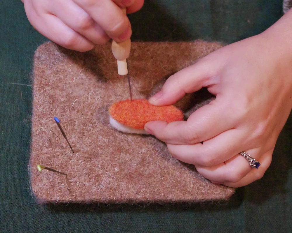 Orange wool on top of white wool with a felting needle going through both to join the two needle felted pieces together.